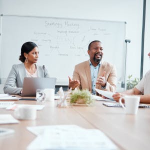 Diverse executive roundtable with seven or eight senior-level professionals sat at a meeting table having an interactive workshop
