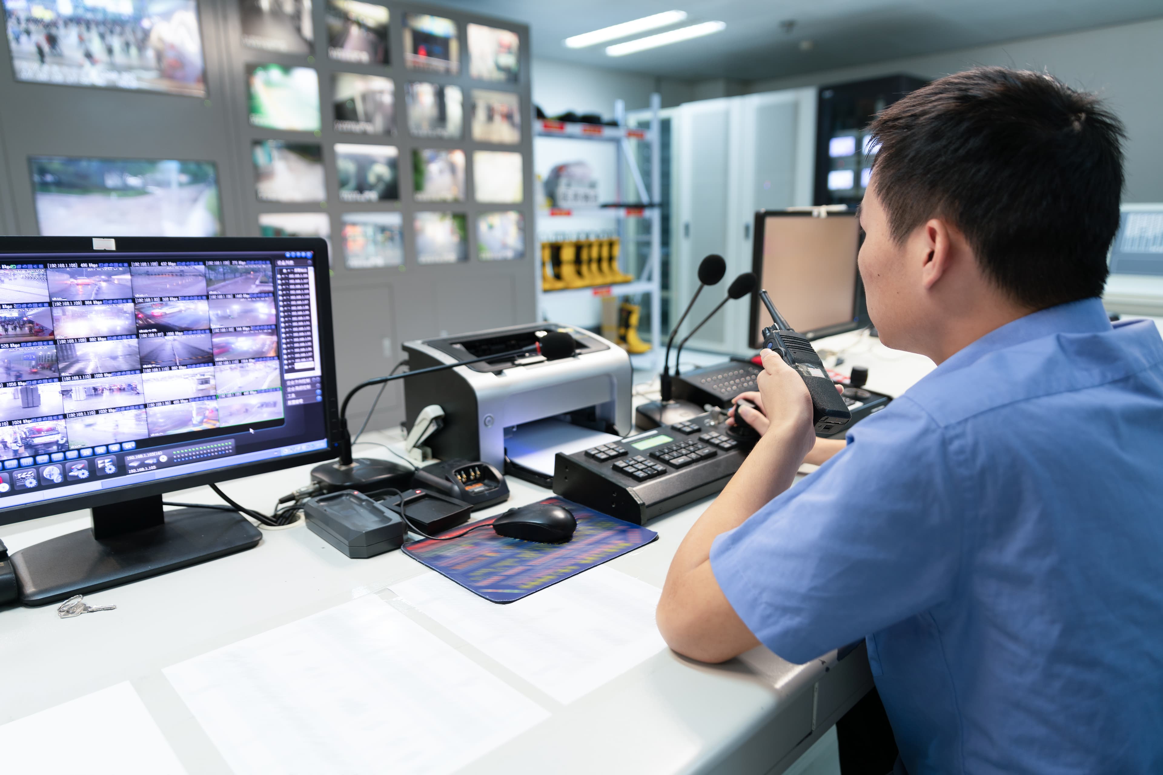 An image of a cleared candidate with a walkie-talkie at a security controls desk in the aerospace and defense industry